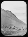 Image of Camp site by hill; sledges on side to tether dogs, igloos [iglus]